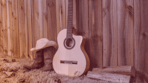 A imagem mostra um par de botas, um chapéu e uma guitarra ao ar livre, com uma cerca de madeira ao fundo. O contexto da imagem está relacionado à música country.